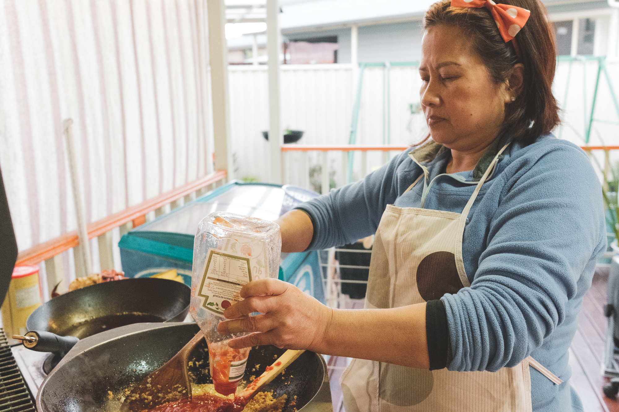 Mum emptying a bottle of tomato sauce into the wok